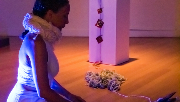 Side view of artist kneeling with stage lighting and art objects in front and in background